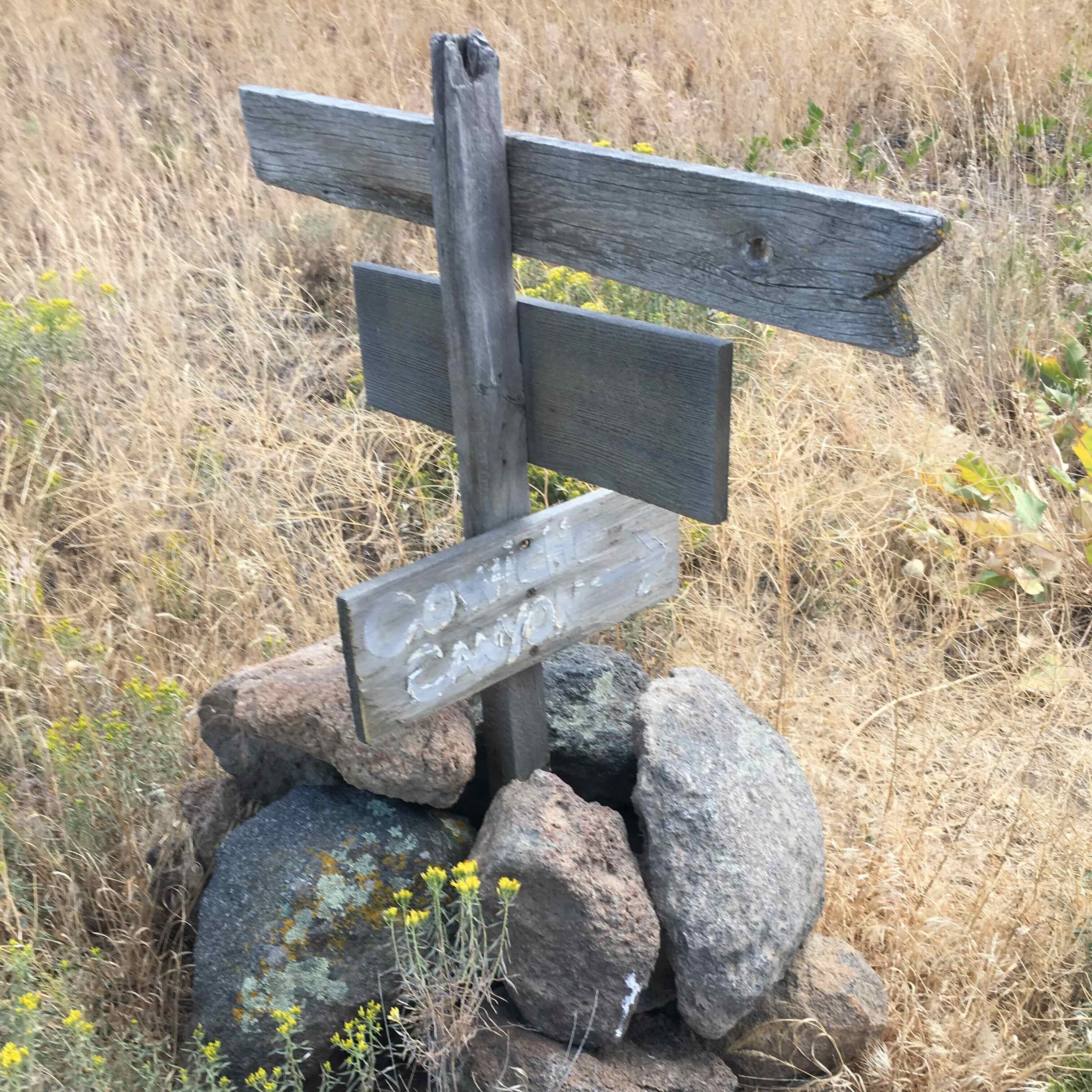 A rock cairn holding a post with three wooden signs pointing in different directions.