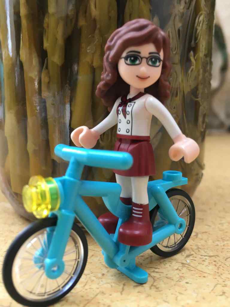Female LEGO figure with brown hair and glasses, on a blue LEGO bike.